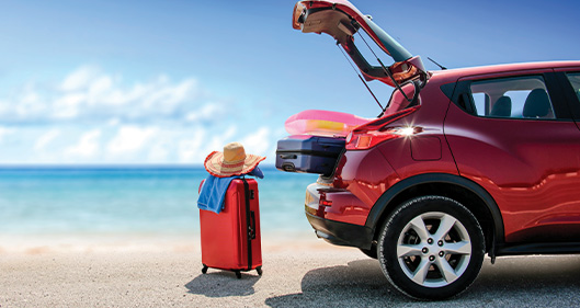 Vehículo rojo con baúl abierto y maletas en la playa 