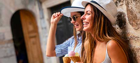 Two young women enjoying ice cream in the sun, wearing white summer hats