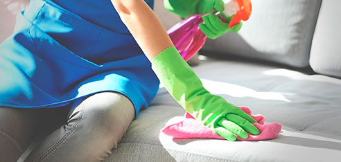 Mujer con guantes color verde limpiando un sofá gris