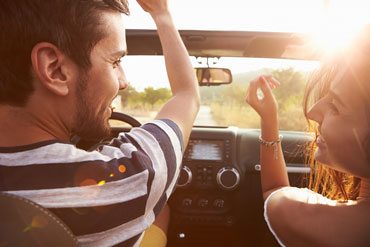 Hombre y mujer sonrientes en el camino dentro de su coche convertible.