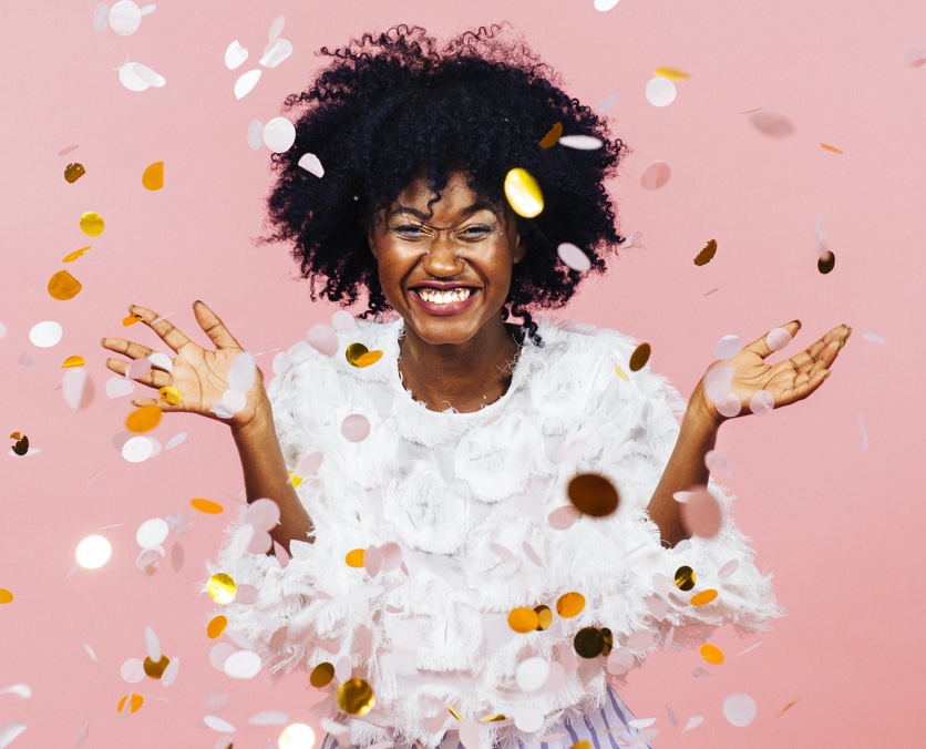 Mujer jóven adulta celebrando y tirando confeti al aire