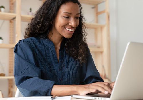 Mujer sonriendo y escribiendo en su computadora portátil