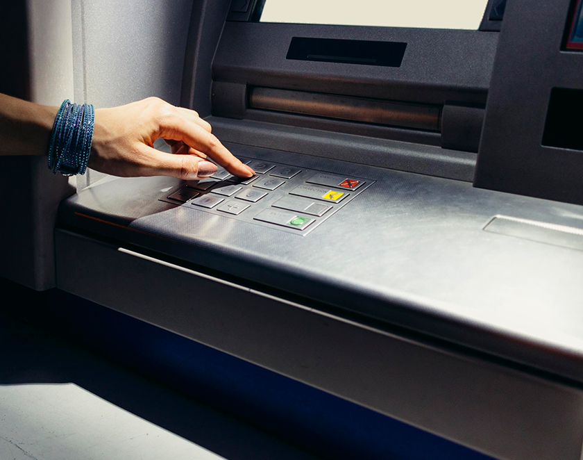 Hand entering its secret pin into a Popular ATM